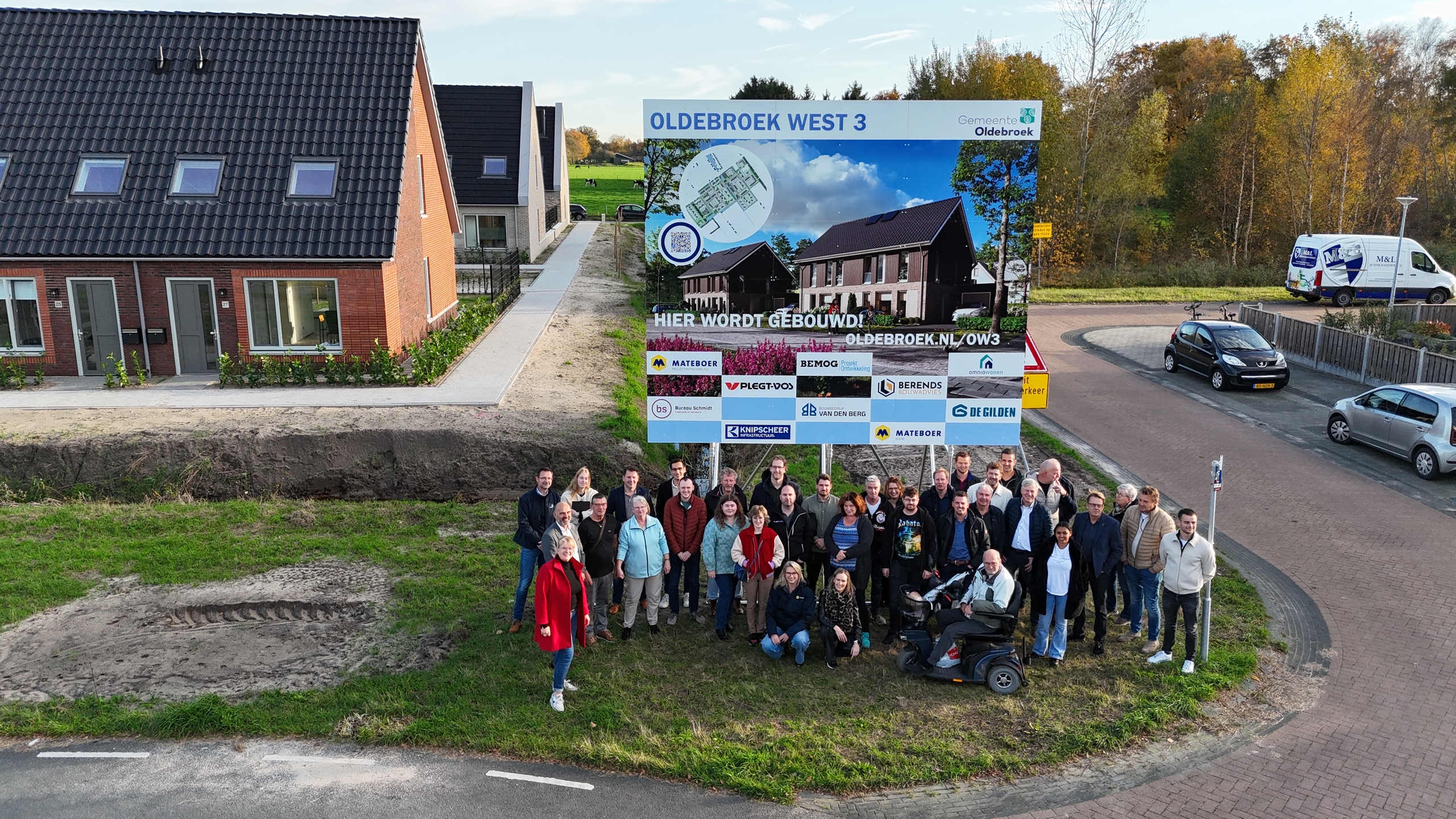 Nieuwe huurders op de foto bij het bouwbord met de gemeente Oldebroek, Omnia Wonen en diverse bouwpartners
